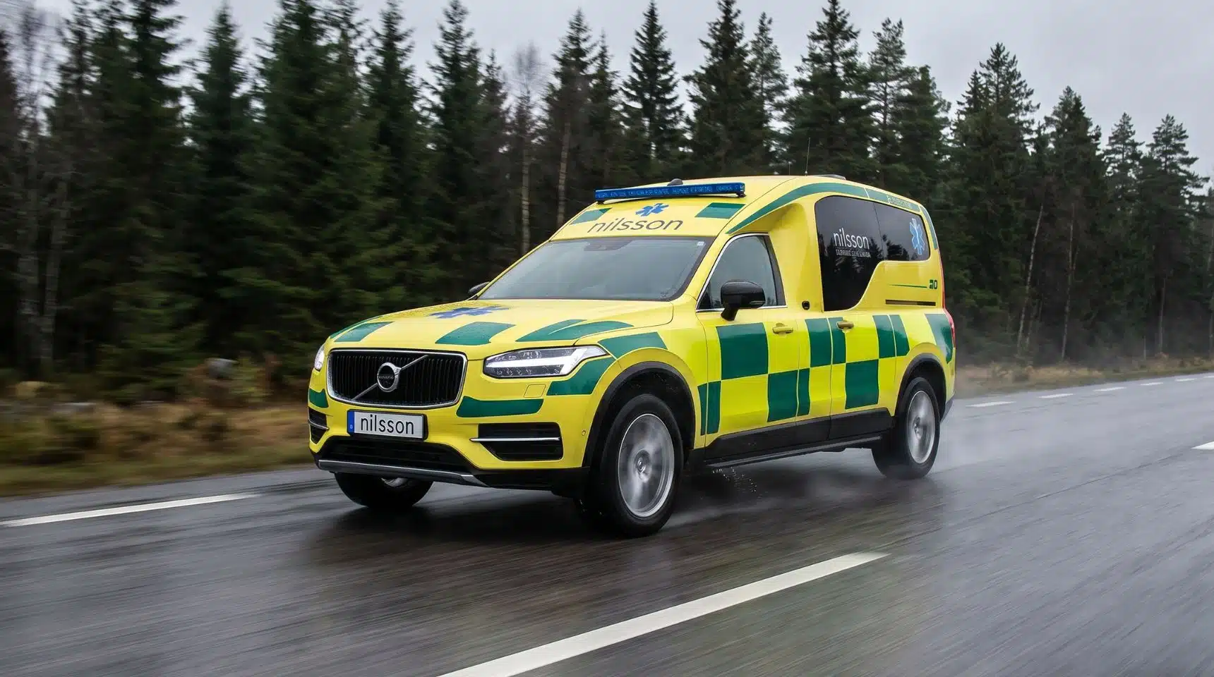 Nilsson XC90 ambulans i gul och grön märkning på en våt väg genom skogen